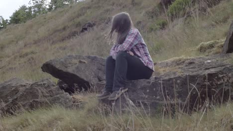 Frau-Sitzt-Auf-Einem-Felsen-In-Rauer-Moorlandschaft