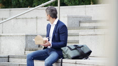 businessman sitting outside on lunch break eating takeaway meal from sustainable recyclable carton