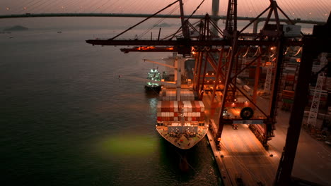 Container-vessel-docked-in-the-port-of-Hong-Kong,-with-traffic-on-a-suspension-bridge-in-the-backdrop