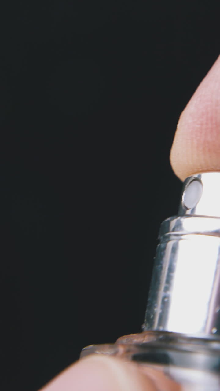 young person sprays women perfume water from little glass bottle on dark background extreme close view