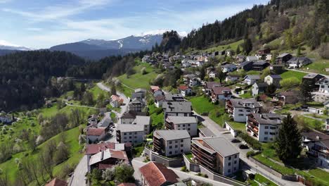 scenic swiss town with hotel apartments on hill with green pasture and snowy mountains in background