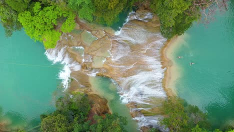 aerial: travellers swimming in tropical waterfall pools, rising top down view