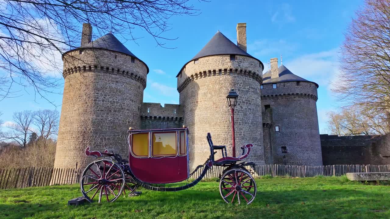En kalesje eller vintage rød hestevogn, parkert på gresset foran steinmurene til middelalderborgen Lassay i Lassay-les-Châteaux, Mayenne i Frankrike.