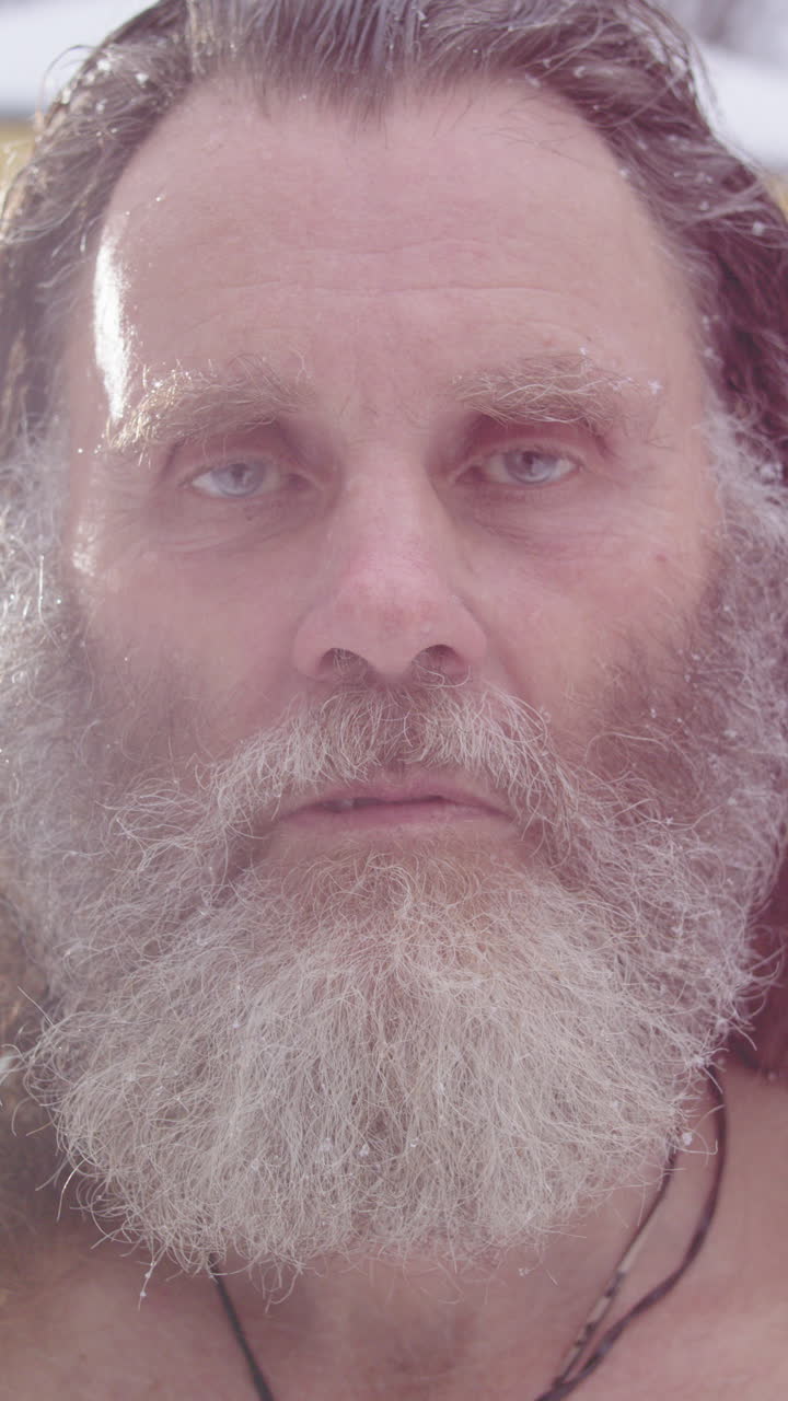 Portrait of bearded wild man with serious facial expression in snow. Vertical