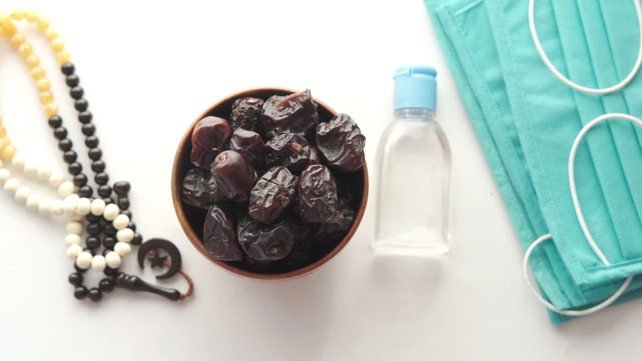 fresh date fruit in a bowl , prayer prayer beads , hand sanitizer and mask on table