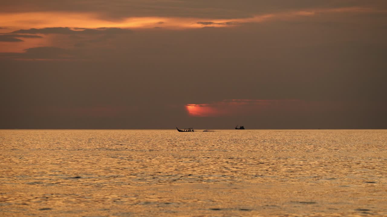 Golden sunset glows across calm ocean waters as distant boats move along the horizon