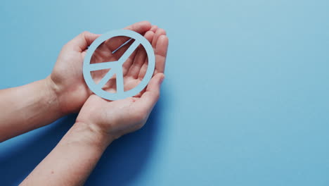 cerca de las manos de una mujer caucásica sosteniendo un signo de paz azul con espacio de copia en un fondo azul