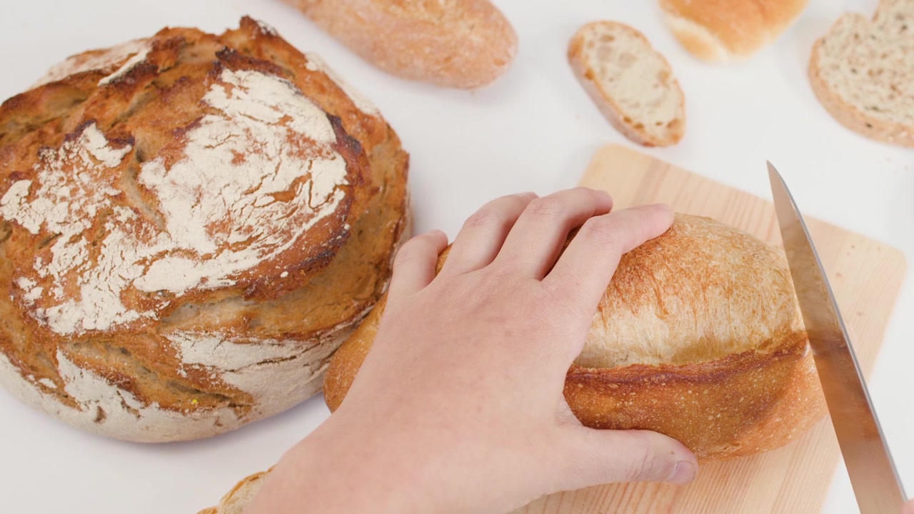 Ripresa dall'alto di mani che usano un coltello per affettare pane artigianale croccante su sfondo bianco