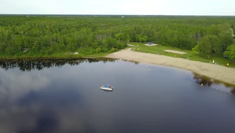 a 4k drone shot flying over a park with a river, capturing people enjoying their time on a boat cruising on the water. a perfect scene for relaxation and leisure.