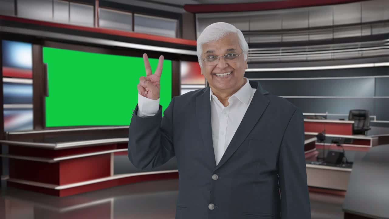 feliz periodista senior indio señalando a la pantalla verde que muestra el signo de la victoria