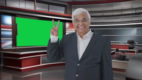 Happy-Indian-senior-journalist-pointing-at-green-screen-showing-victory-sign