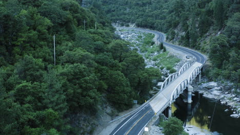 Aerial-flying-backwards-above-rural-road-in-valley-with-green-trees-and-river