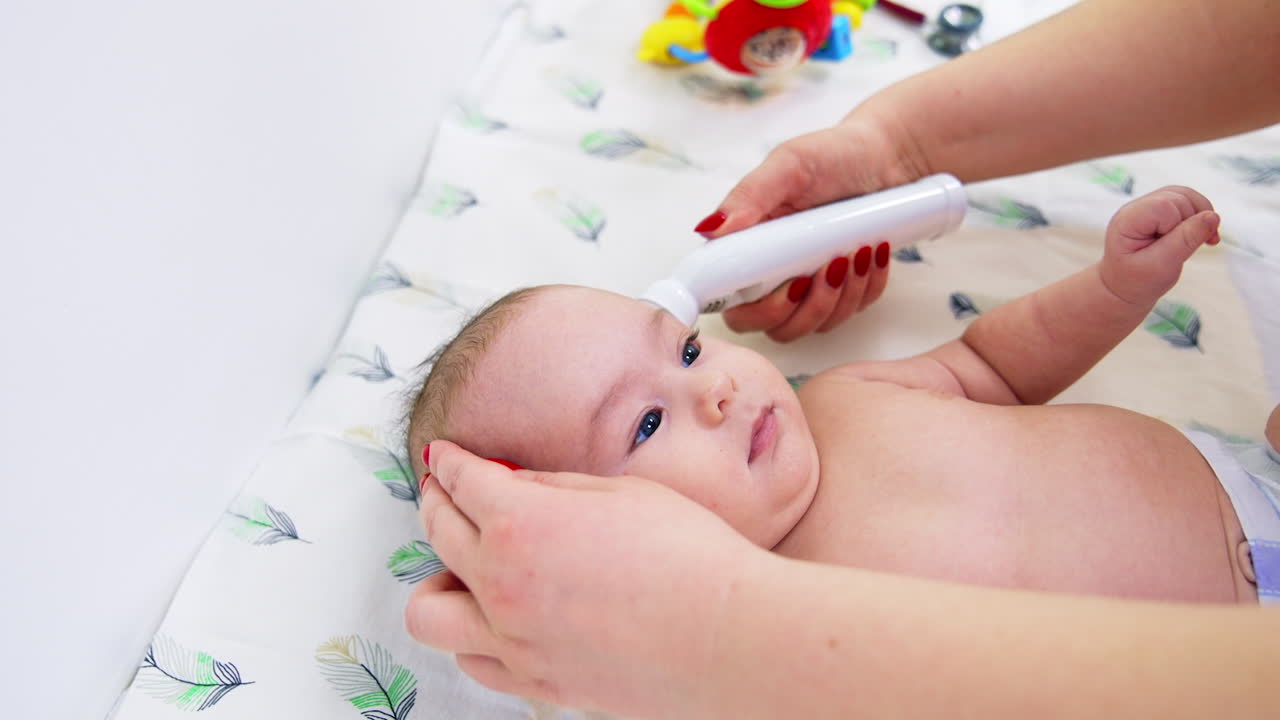Caucasian infant boy lying on the doctor's table. Pediatrician takes baby's temperature with electric thermometer. Close up.