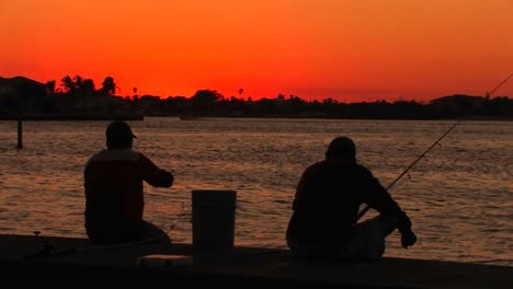 Die-Silhouette-Von-Zwei-Männern,-Die-Bei-Sonnenuntergang-Angeln