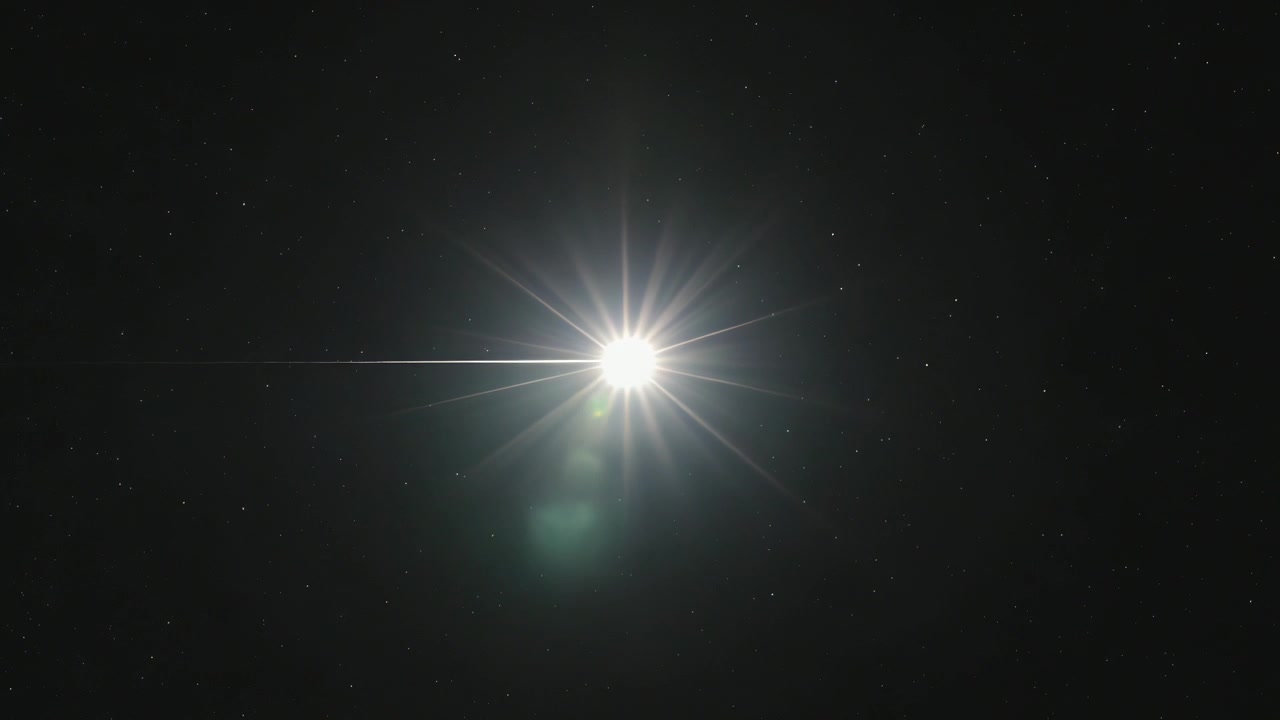 Entrando por la izquierda, una fuente de luz brillante se mueve hacia la derecha a través de las estrellas debido al movimiento de la cámara, creando destellos de lente vívidos.