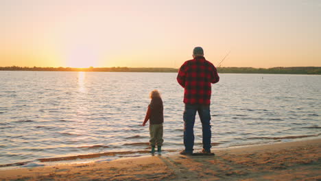 rest on river shore in summer sunset old fisher and his grandson are fishing in evening rear view