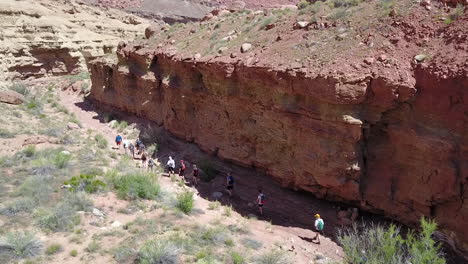 Drone-view-of-hikers-in-single-file-in-ravine-next-to-sandstone-cliff