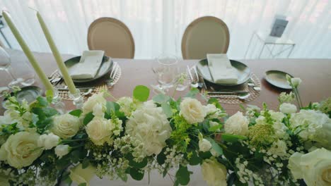 luxury wedding sweetheart table with white roses and greenery by sunlit sheer curtains