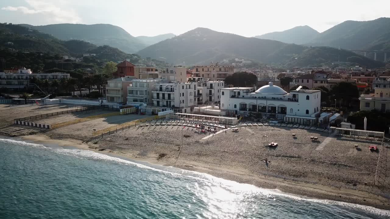 Panning shot of a Mediterranean town with a sandy beach during a sunset. Italy, aerial drone clip