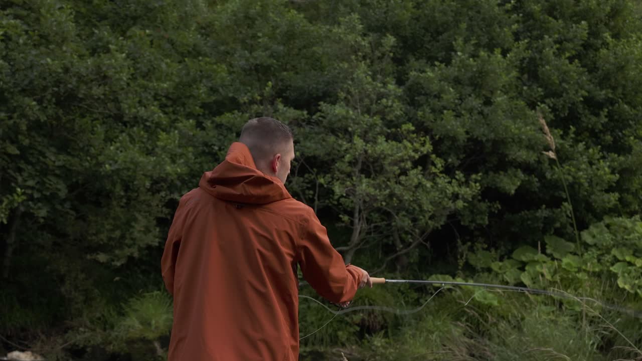 Slowmotion-optagelse af en fisker, der fluefisker og kaster sin line ud i floden.