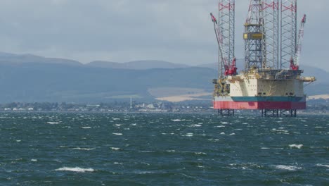 stationary offshore oil platform in rough sea, panning shot with scottish hills and overcast sky