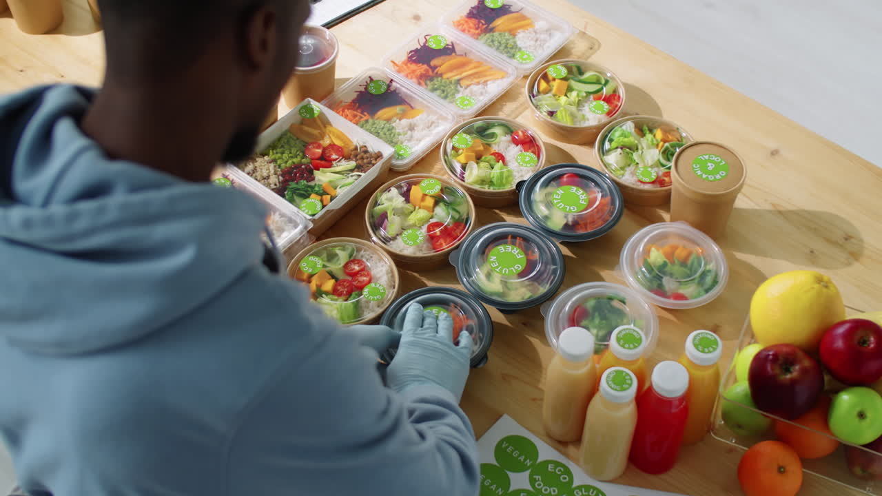 trabajador masculino negro aplicando pegatinas en contenedores con comidas saludables