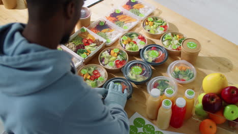 black male worker applying stickers on containers with healthy meals