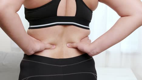 adult woman is holding her lower back while standing and suffering from unbearable pain and self massage by her hand