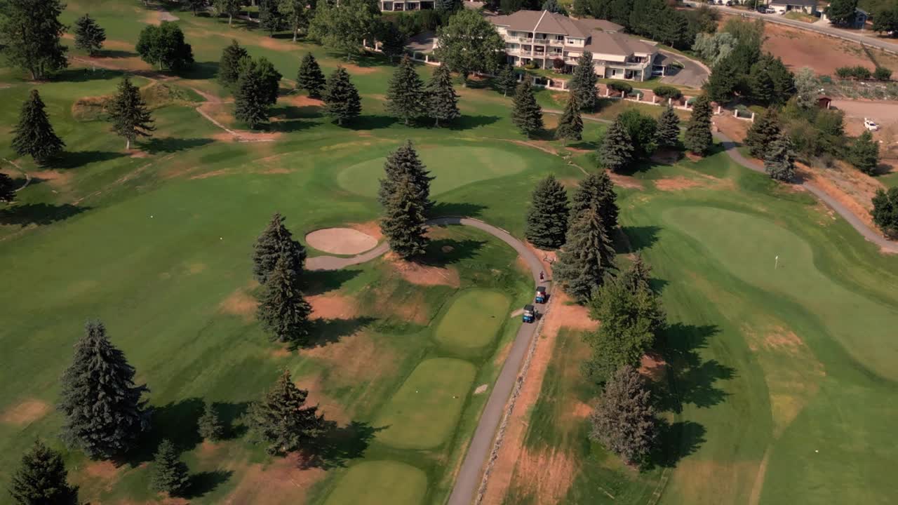 Aerial High angle looking down two golf carts parked on gravel road leading through lush green course filled with trees putting green fairway Kelowna BC Shannon Lakes Golf Course