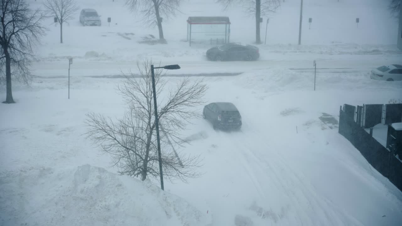 Car turns from building parking lot to road in heavy snow storm