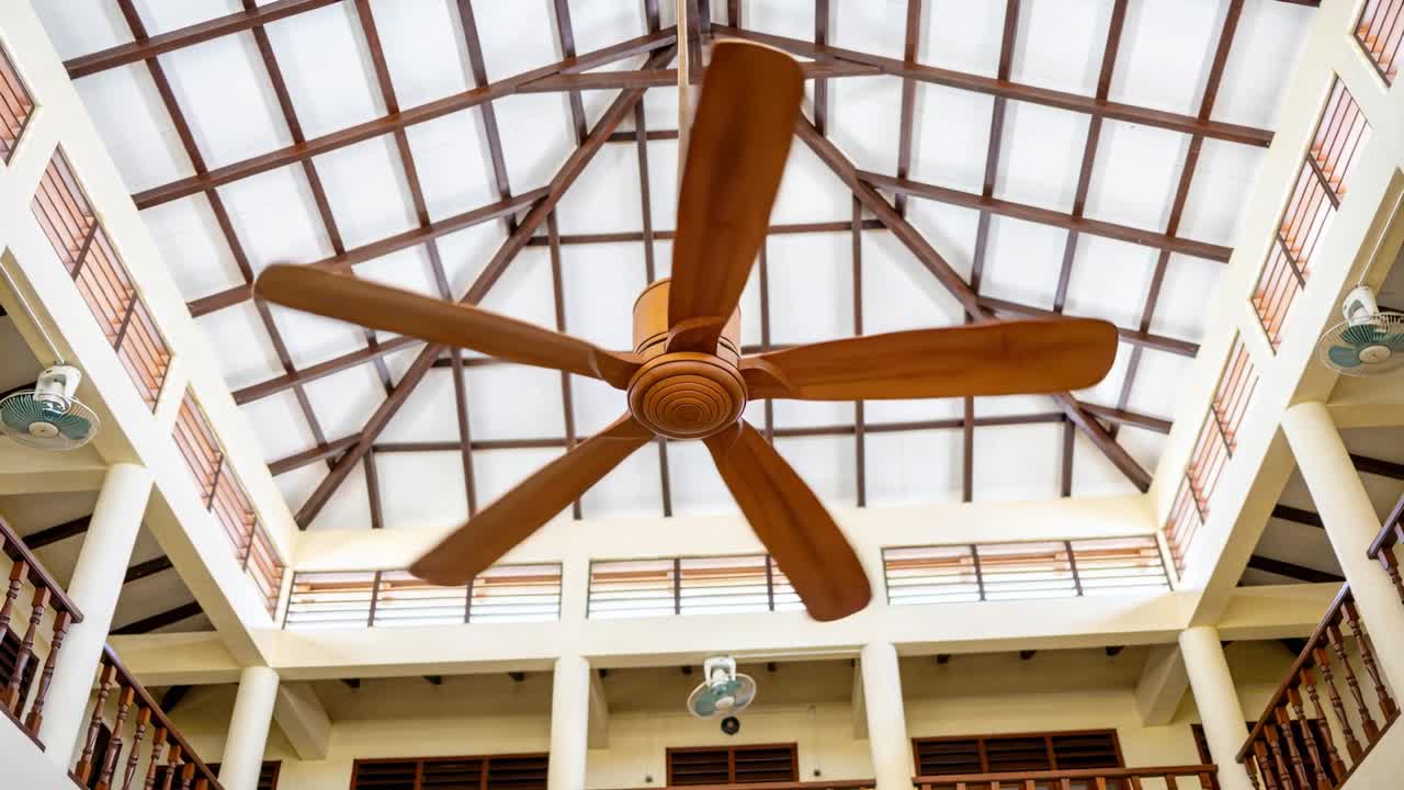 Vertical video: Motor running large wooden fan rotating in atrium for cooling, showing small fans