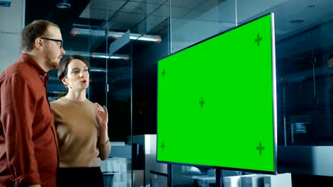 late at night male and female specialists in conference room have discussion about mock-up chroma key green screen tv.