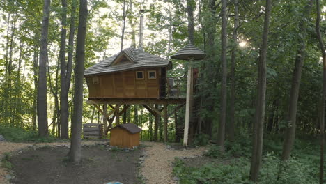 Zooming-4k-shot-of-a-luxurious-treehouse-in-Dolní-Morava,-Czech-Republic-in-the-middle-of-a-forest-with-a-campsite-and-a-campfire-burning-below