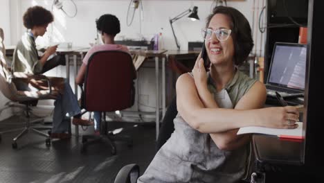 happy caucasian female worker talking on smartphone in jewellery studio in slow motion