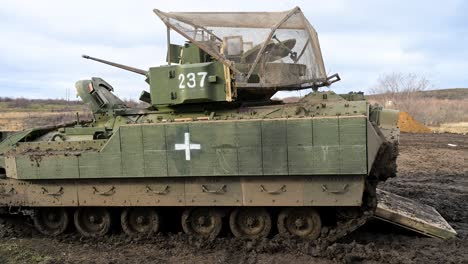 A US-made M2 Bradley, marked as a medical evacuation vehicle, navigates muddy terrain in Ukraine. It is fitted with a 'cope cage' for protection against drone attacks