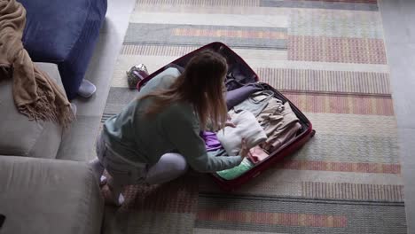 A-woman-in-a-hotel-room-puts-things-in-a-suitcase,-high-angle-view