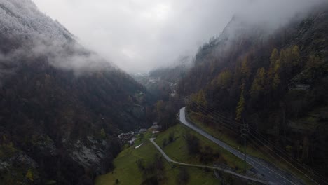 Video-De-Drones-Voladores-Giratorios-Hacia-Adelante-Tranquilos-A-Través-Del-Valle-Nublado-De-Los-Alpes-Suizos-En-Una-Tarde-De-Invierno-Malhumorada-Con-Bosques-De-Pinos-Exuberantes-Y-Hermosos-árboles-Nevados-En-Las-Montañas-Con-Camino-En-Medio-Del-Valle