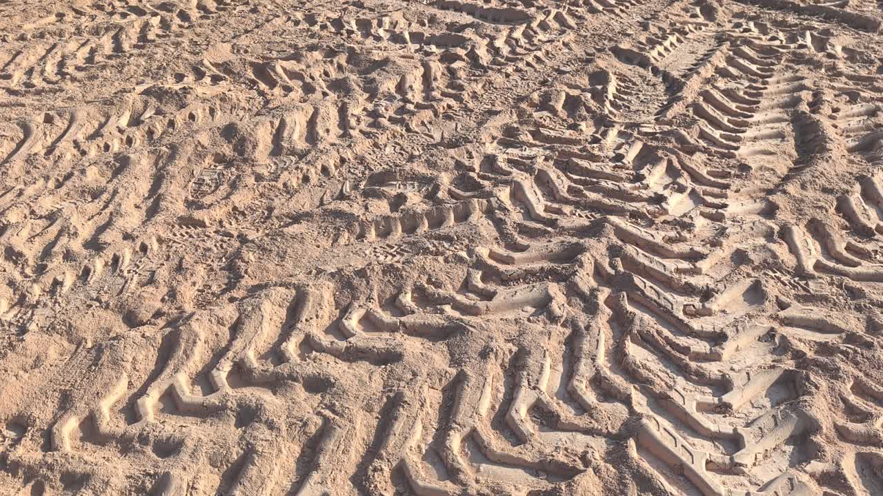 View of intricate tire patterns imprinted on soft earth. The golden-yellow soil creates a textured landscape of dusty trails left by passing vehicles