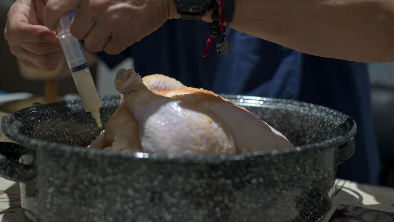 Close up of a mature man hands injecting a raw turkey in a cooking pot preparing of christmas thanksgiving
