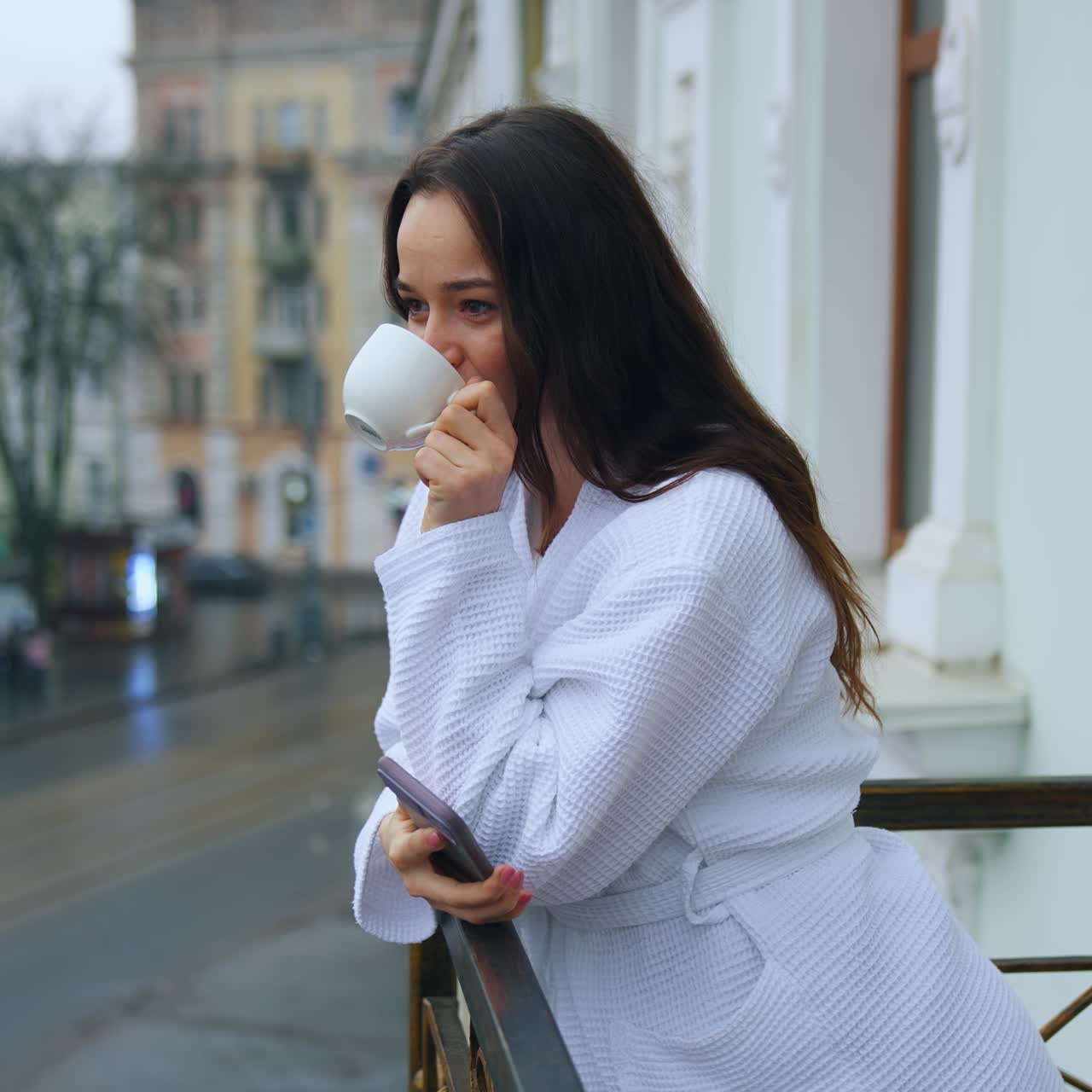 Beautiful young girl in a snow-white terry bathrobe on a balcony with the cup of tea in the morning. Happy holidays away from home. Woman in hotel