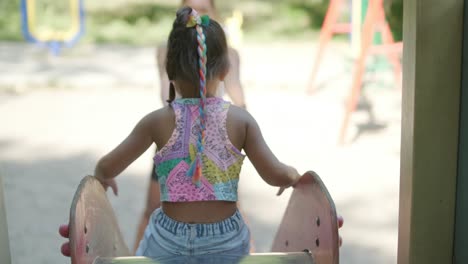 madre embarazada viendo a su hija jugar en el tobogán en el patio de recreo