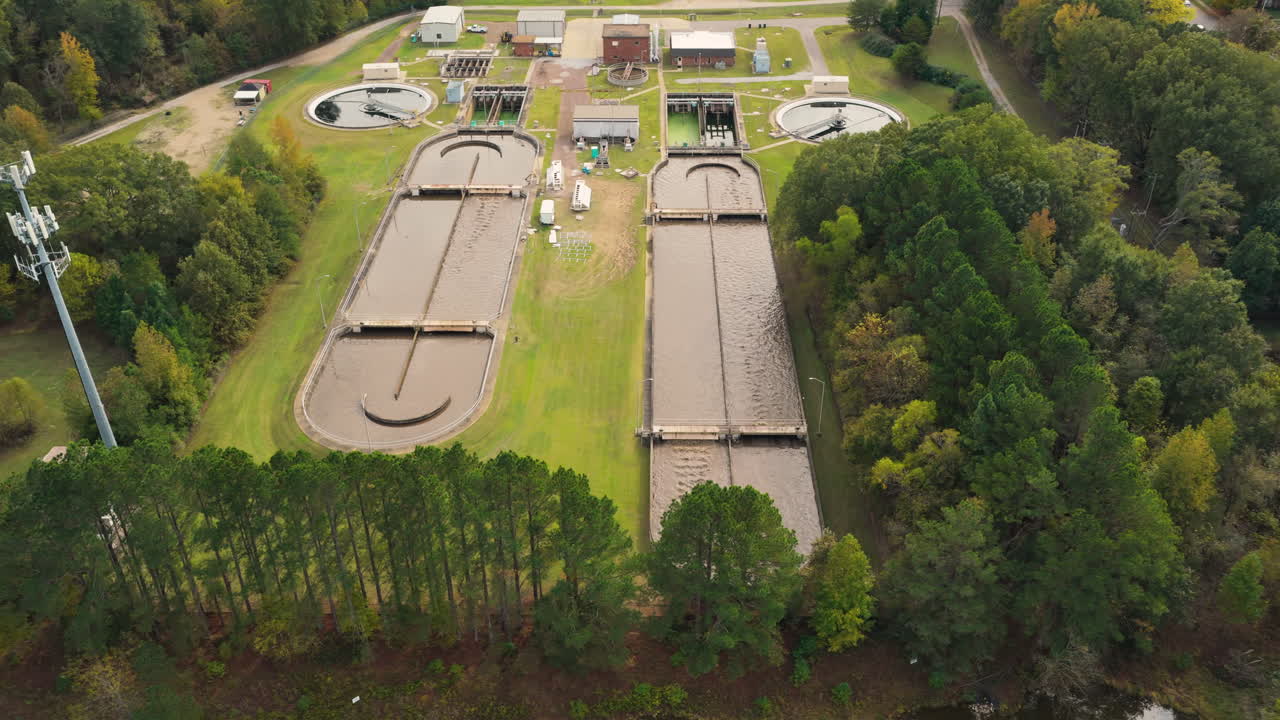 Wastewater treatment facility basins surrounded by trees, large long pools to circulate clean and filter, aerial tracking right