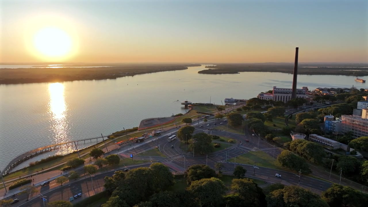 Scena del lungofiume di Porto Alegre al tramonto con l'Usina do Gasômetro e riflessi dorati sul fiume Guaíba.
