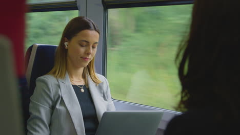 businesswoman with wireless earbuds commuting to work on train working on laptop