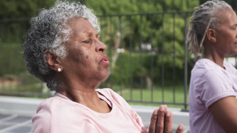 Senior-african-american-female-friends-practicing-yoga-meditation-sitting-on-balcony,-slow-motion