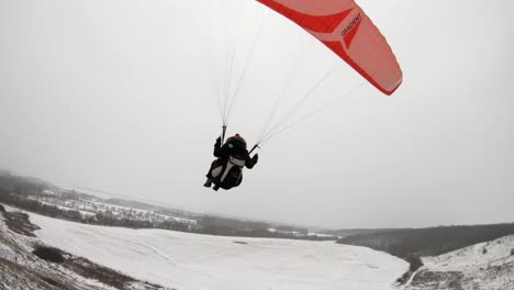 Drone-Siguiendo-De-Cerca-El-Parapente-Durante-El-Aterrizaje-Y-La-Nevada