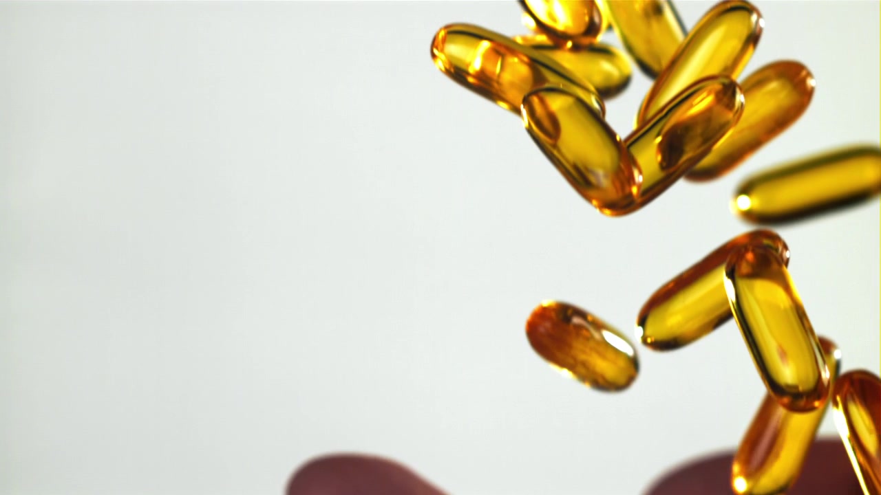Capsule Omega 3 dorate che cadono in una mano al rallentatore