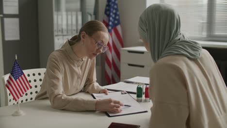 Female Visa Officer Explaining How to Fill Out Application Form to Muslim Woman