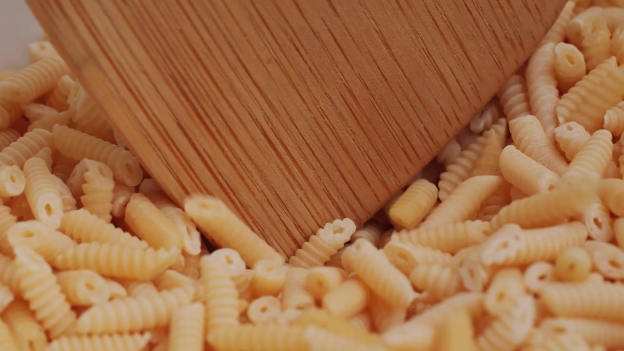 Primo piano di pasta secca mescolata con un cucchiaio di legno