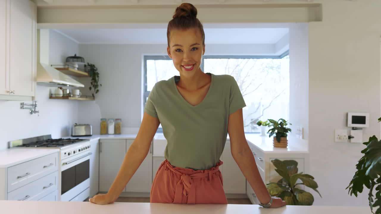 Donna sorridente in una cucina moderna che si gode la luce del sole mattutina attraverso la finestra, a casa.